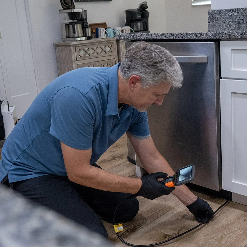 Kit Brucker kneeling at a kitchen cabinet with a borescope
