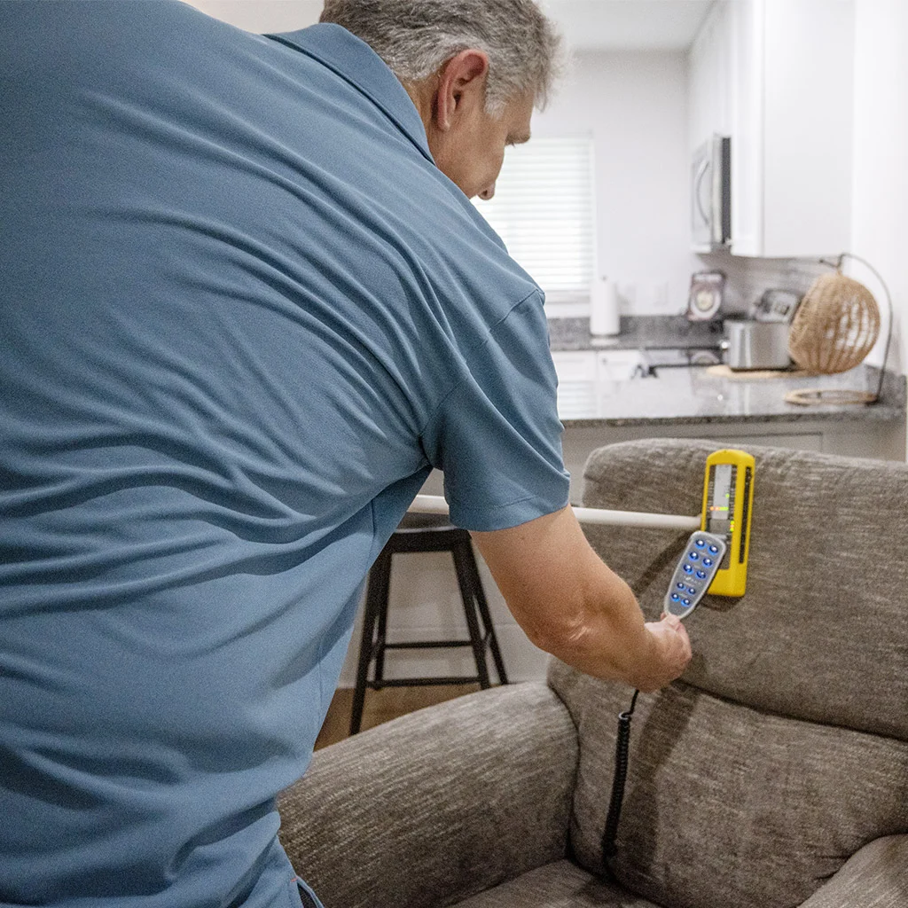 Kit Brucker holding a meter beside a living room sofa